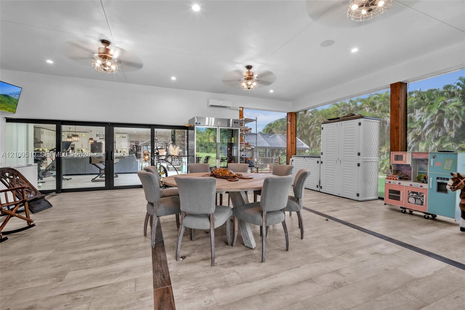 Expansive covered outdoor living area featuring wood-finish flooring, recessed lighting, ceiling fans, and black-framed glass wall systems