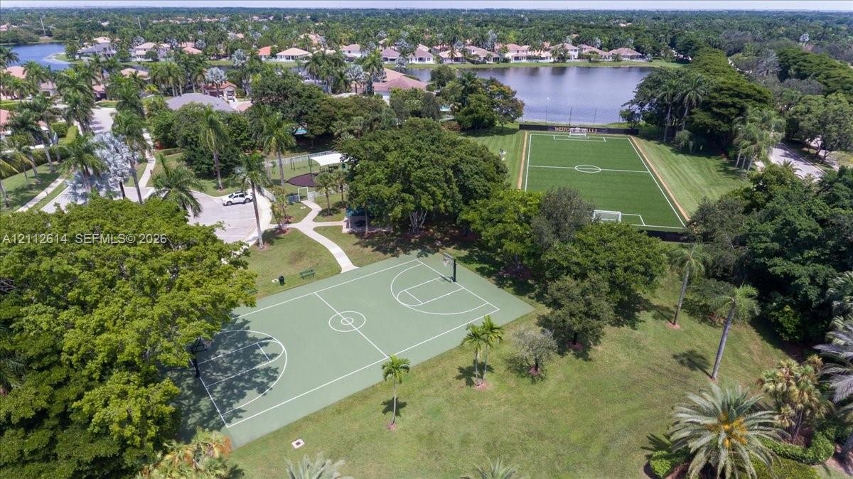 Recreational park featuring a full-size basketball court, synthetic turf soccer field, paved pathways, and mature canopy trees