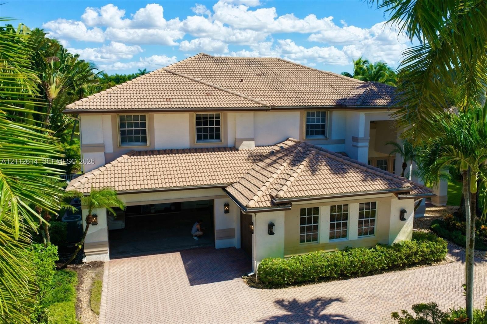 Two-story stucco exterior featuring a multi-hipped tile roof, paver driveway, multi-car garage, and grid-pattern window panes