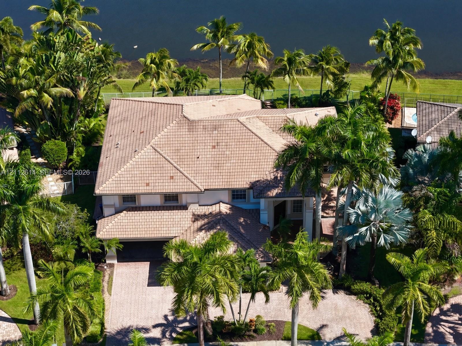Multi-level residence featuring a tile roof, paved driveway, and mature landscaping on a waterfront lot