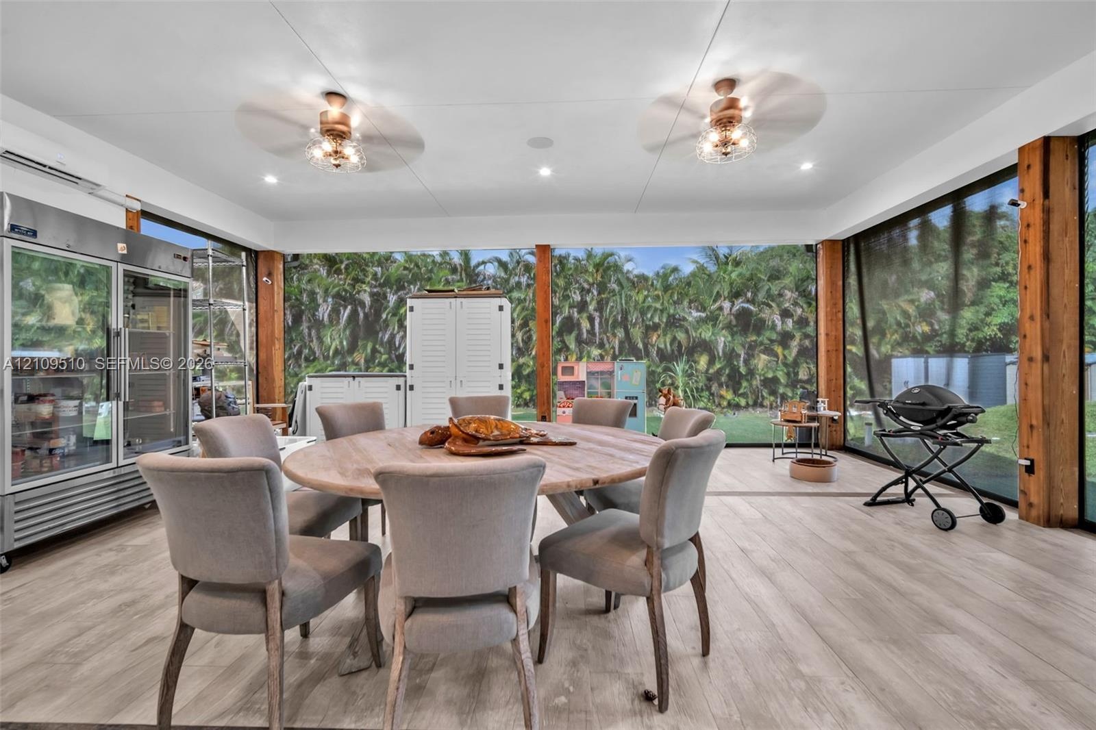 Enclosed outdoor living space featuring wood-finish flooring, exposed wood support pillars, dual ceiling fans, and an integrated stainless steel glass
