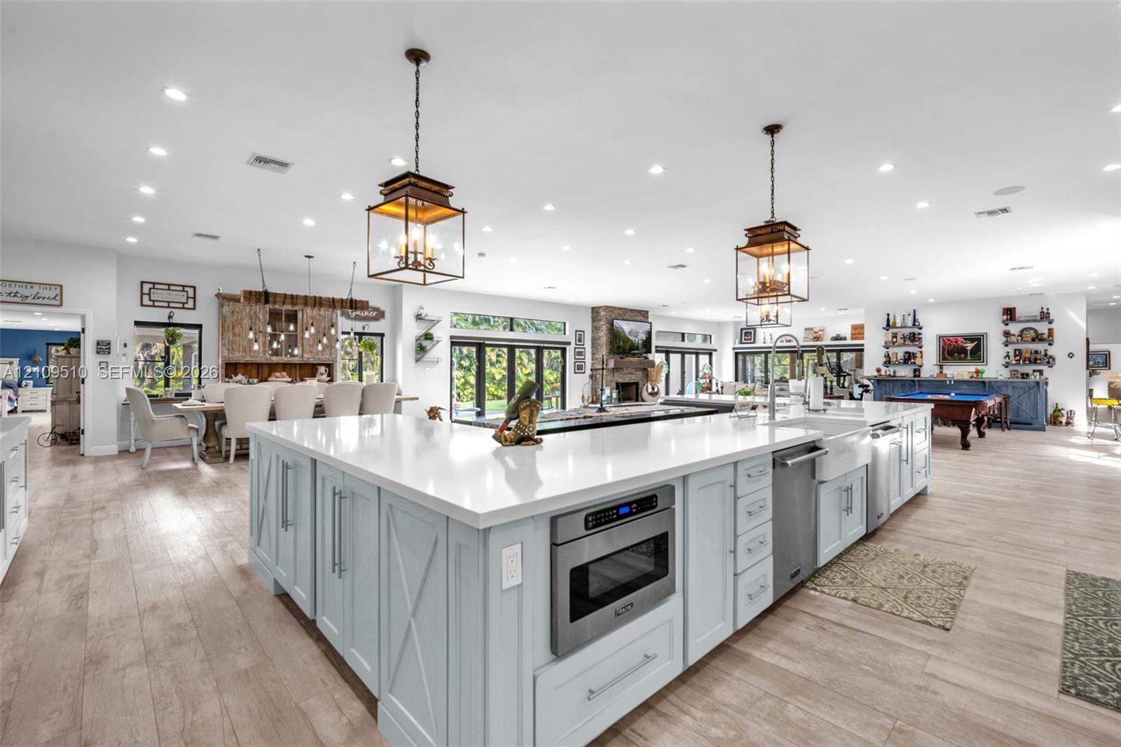 Large kitchen island featuring light blue cabinetry, quartz countertops, farmhouse-style sink, built-in microwave, and wood-finish flooring throughout