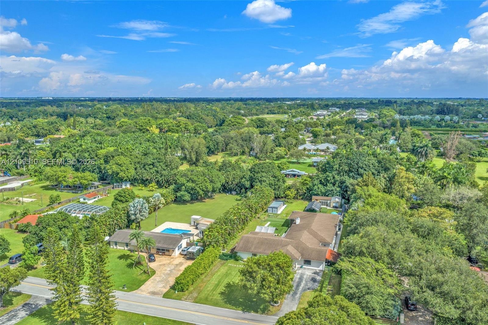Aerial perspective of extensive acreage featuring a swimming pool, paved driveway, mature trees, and landscaping