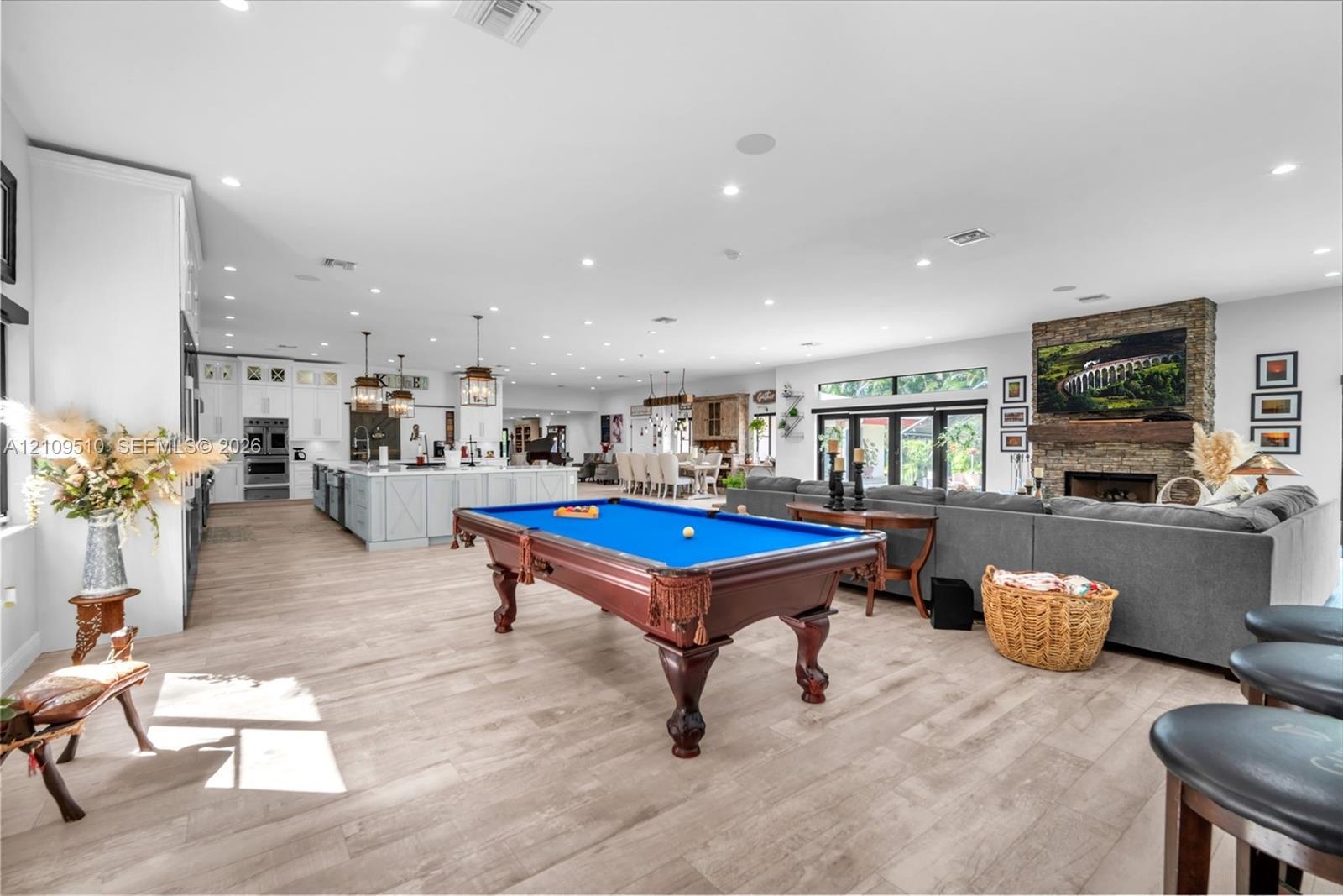 Open-concept interior featuring wood-finish flooring, recessed lighting, a stone-faced fireplace with a timber mantel, and a kitchen island with penda