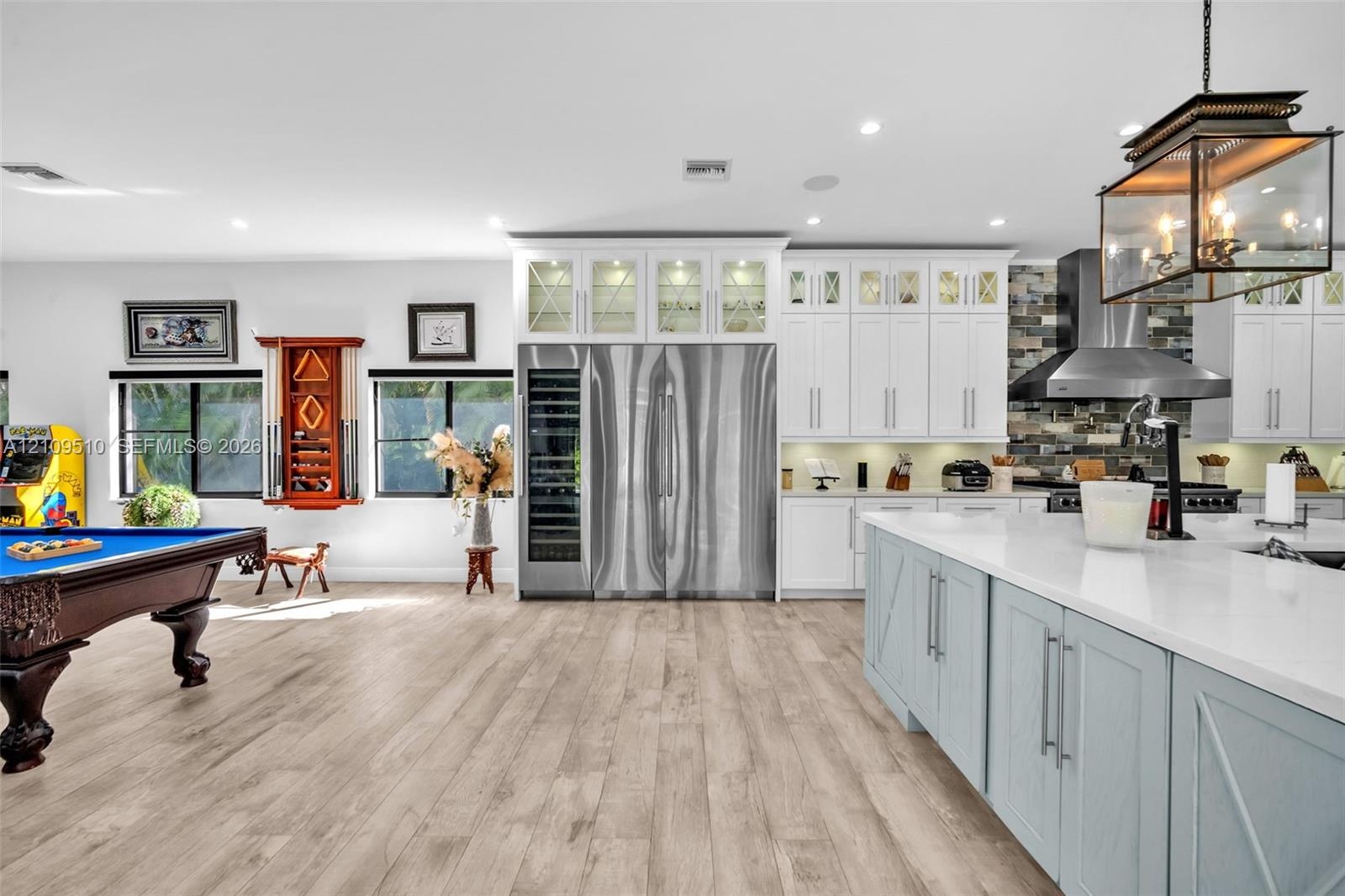 Kitchen featuring custom white cabinetry with glass-front uppers, a stainless steel side-by-side refrigerator, a built-in wine cooler, a stone tile ba