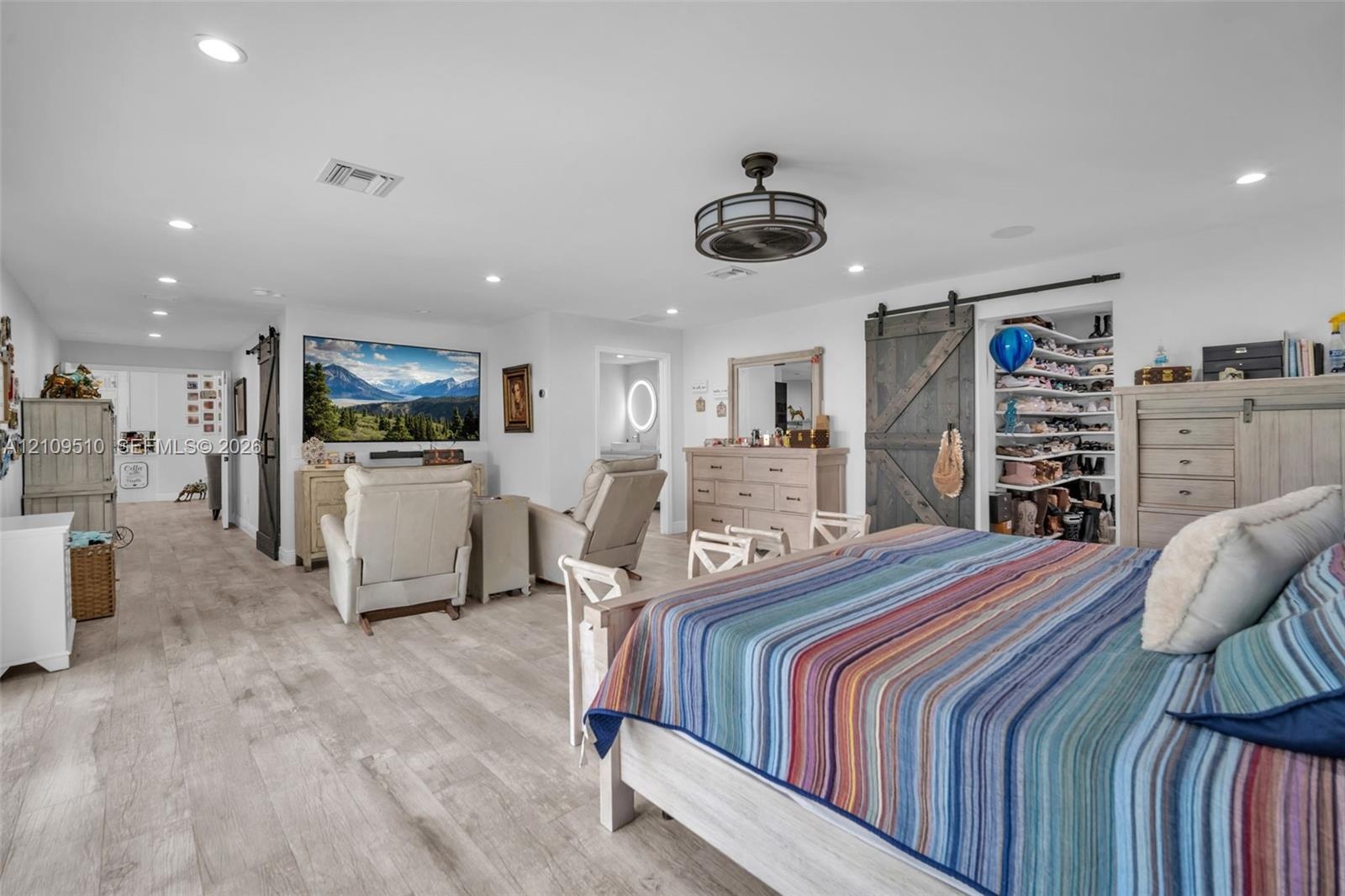 Wood-finish flooring, recessed lighting, ceiling fan with light fixture, and dark-toned sliding barn-style doors