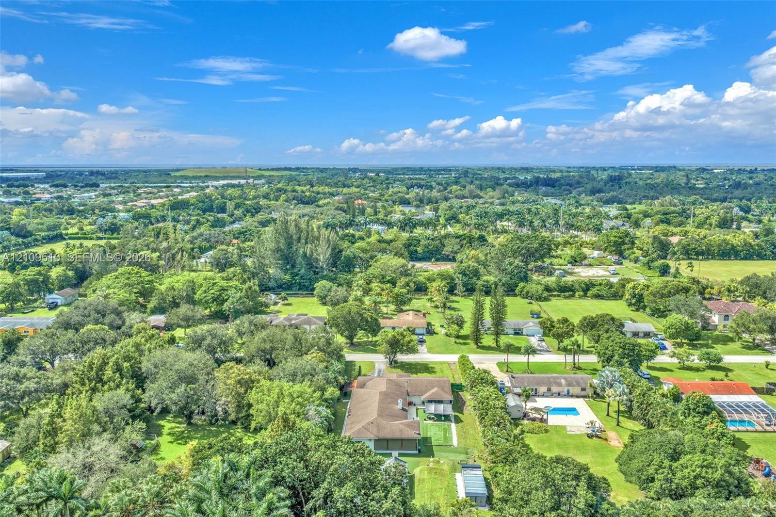 Aerial perspective featuring expansive acreage, mature tree canopy, residential structure with a shingled roof, and vast green space