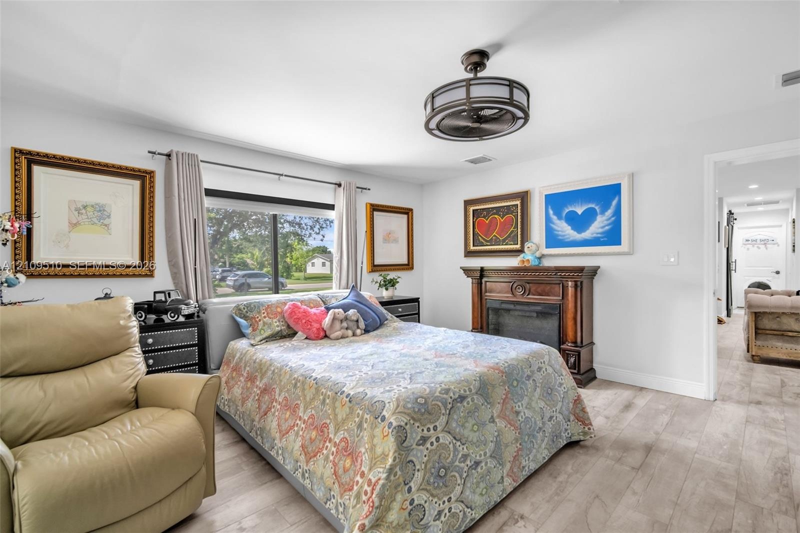 Wood-finish flooring, fireplace with a decorative wooden mantel, and a multi-blade ceiling fan with a circular cage housing