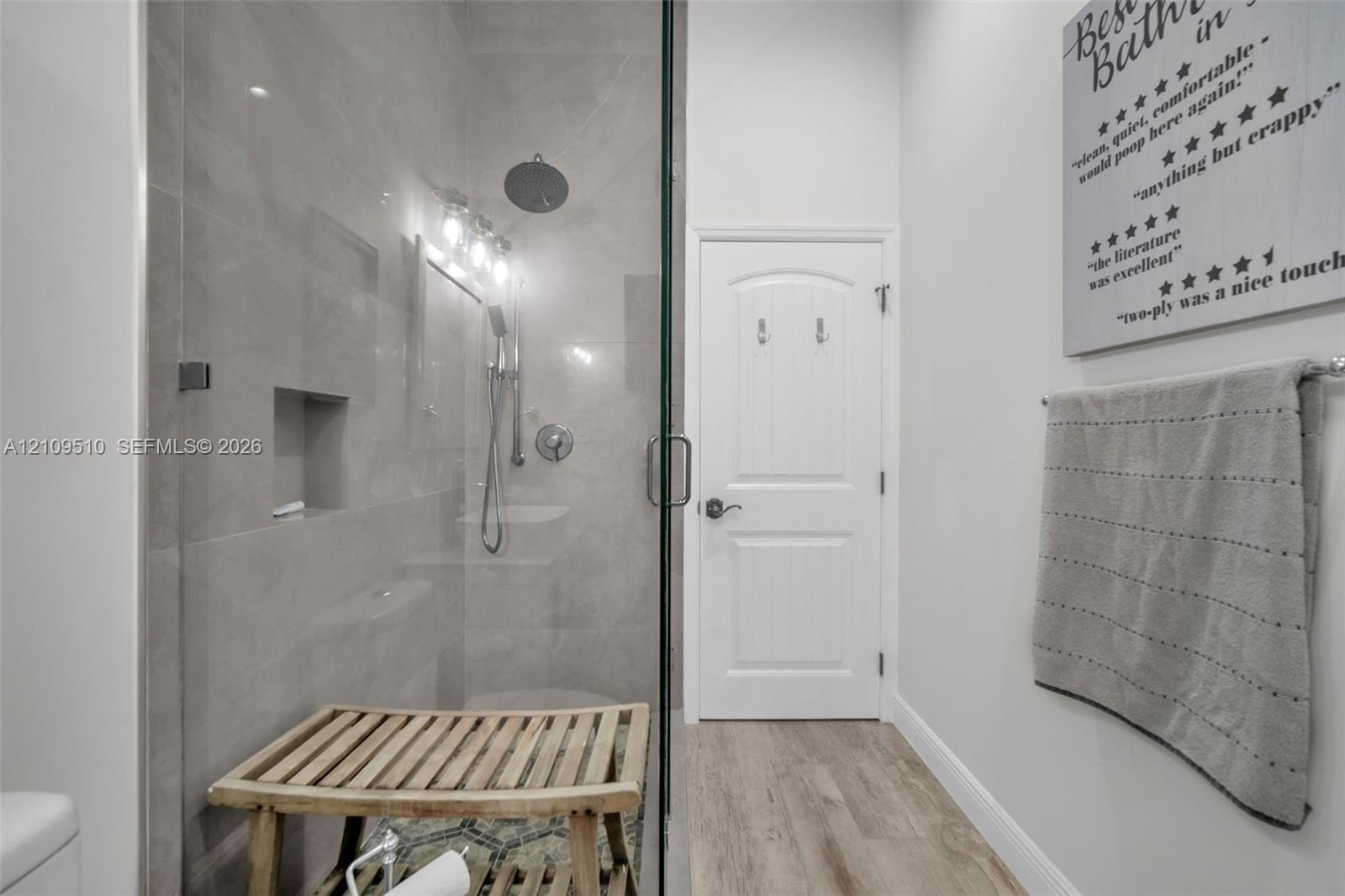Walk-in shower featuring oversized tile walls, a recessed wall niche, a ceiling-mounted rainfall shower head, and a frameless glass door, complemented