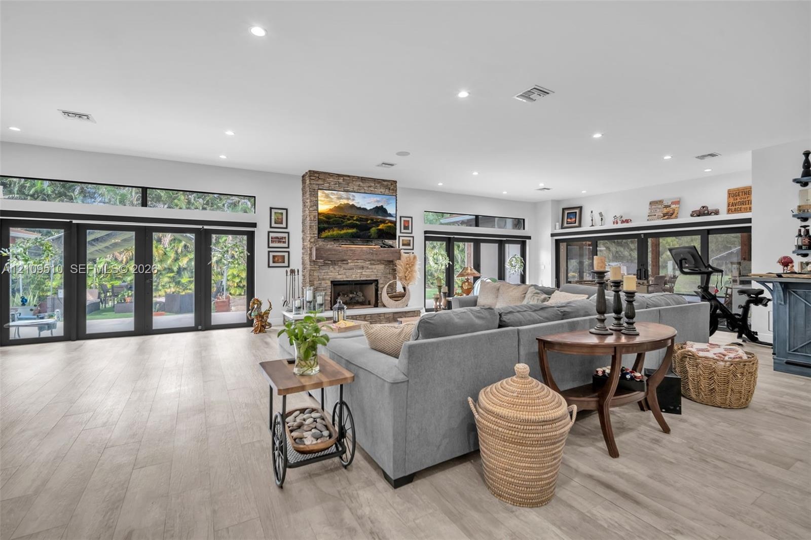 Open-concept living space featuring wood-finish flooring, recessed lighting, floor-to-ceiling multi-panel glass doors, and a floor-to-ceiling stone-su
