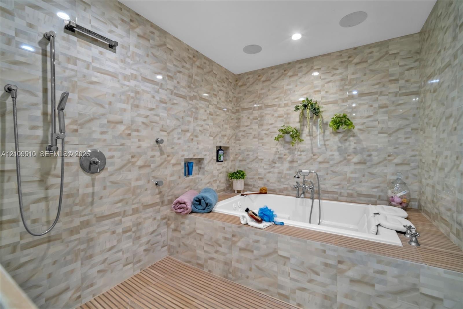 Walk-in wet room featuring textured tile walls, a deep soaking tub with chrome hardware, an integrated shower system with a handheld sprayer, built-in