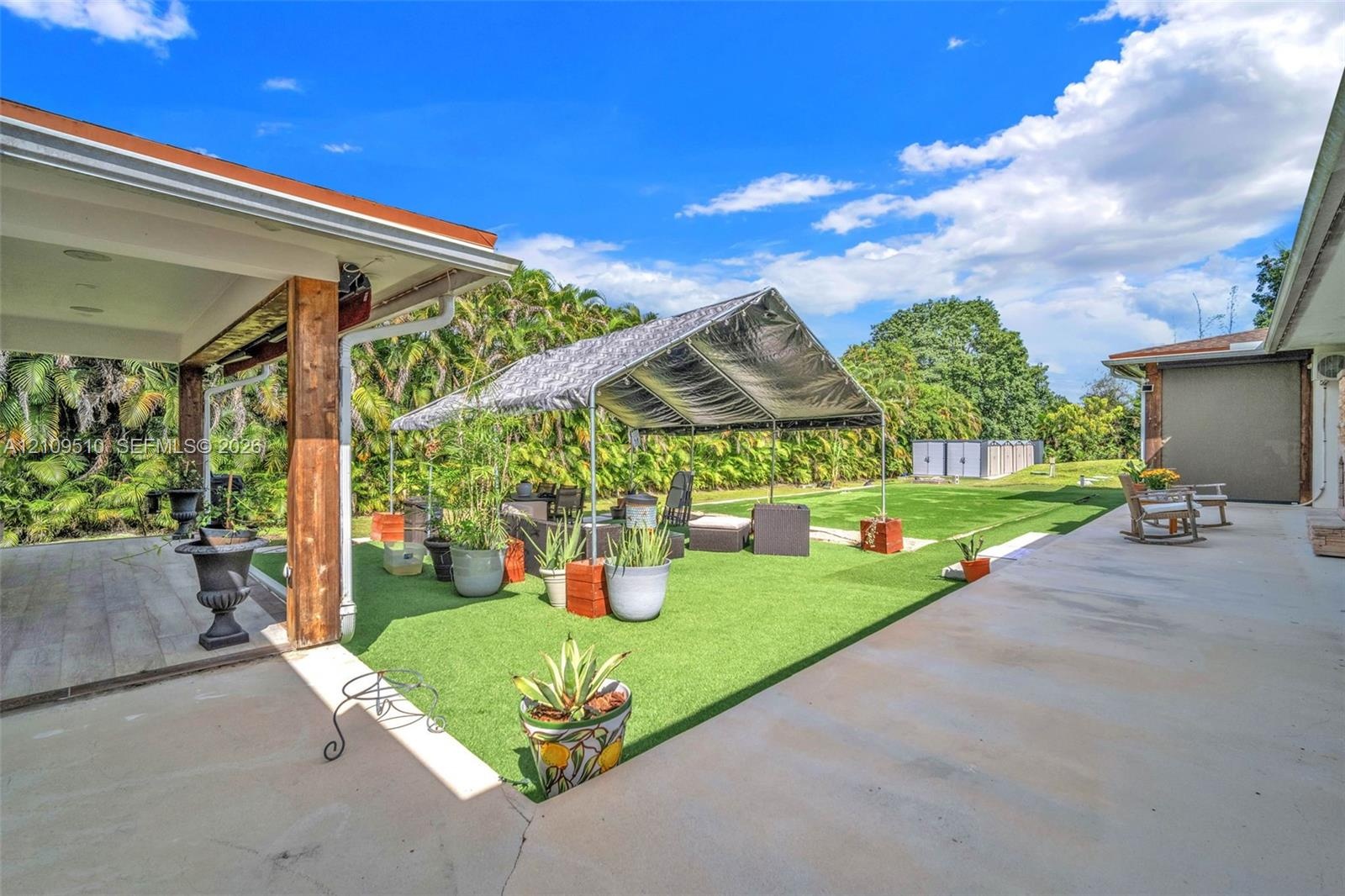 Covered patio with wood-post supports, expansive artificial turf grounds, and concrete paved perimeter