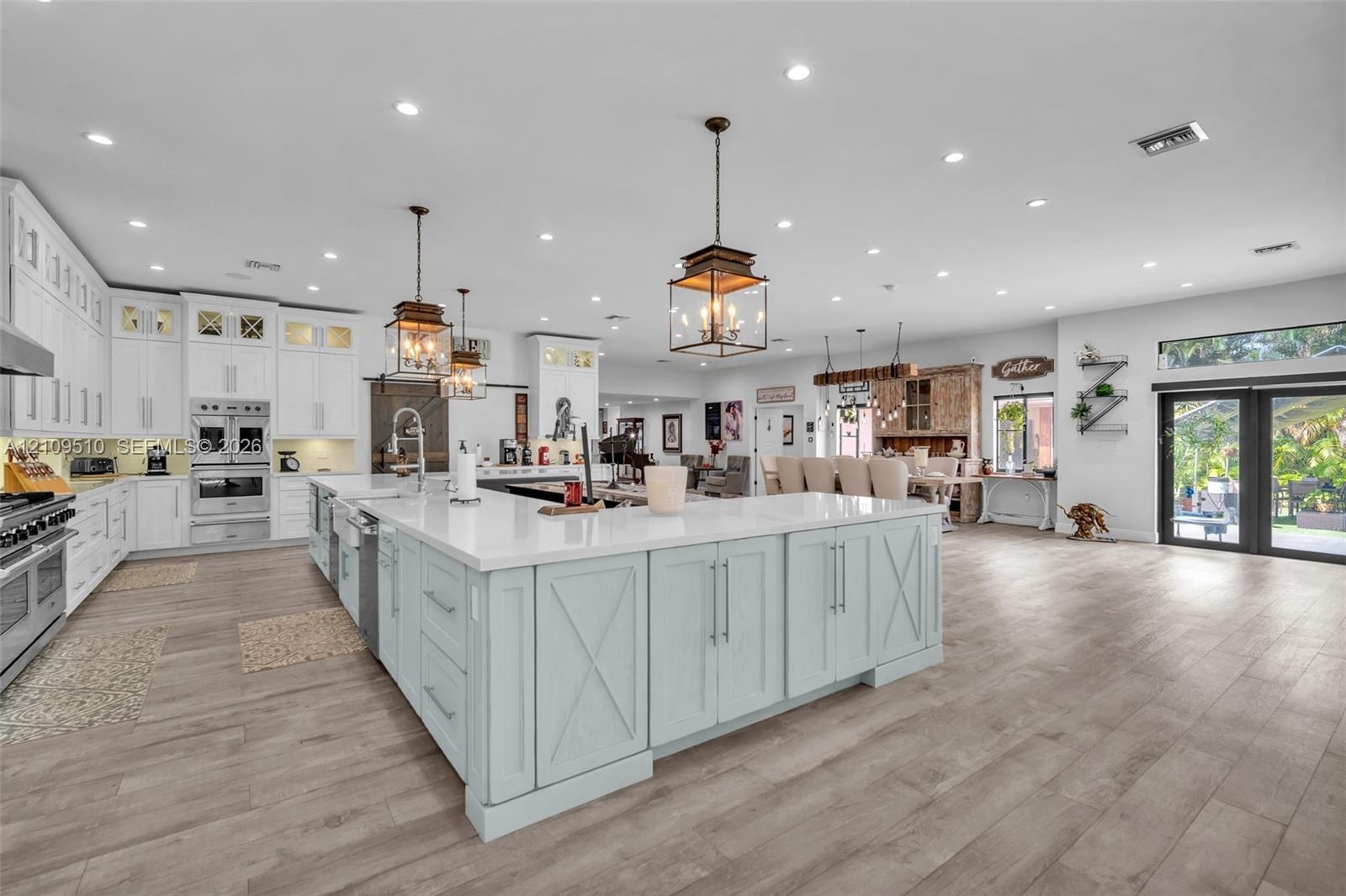 Open-concept kitchen featuring an expansive center island with stone countertops, white cabinetry, integrated stainless steel appliances, and wood-fin