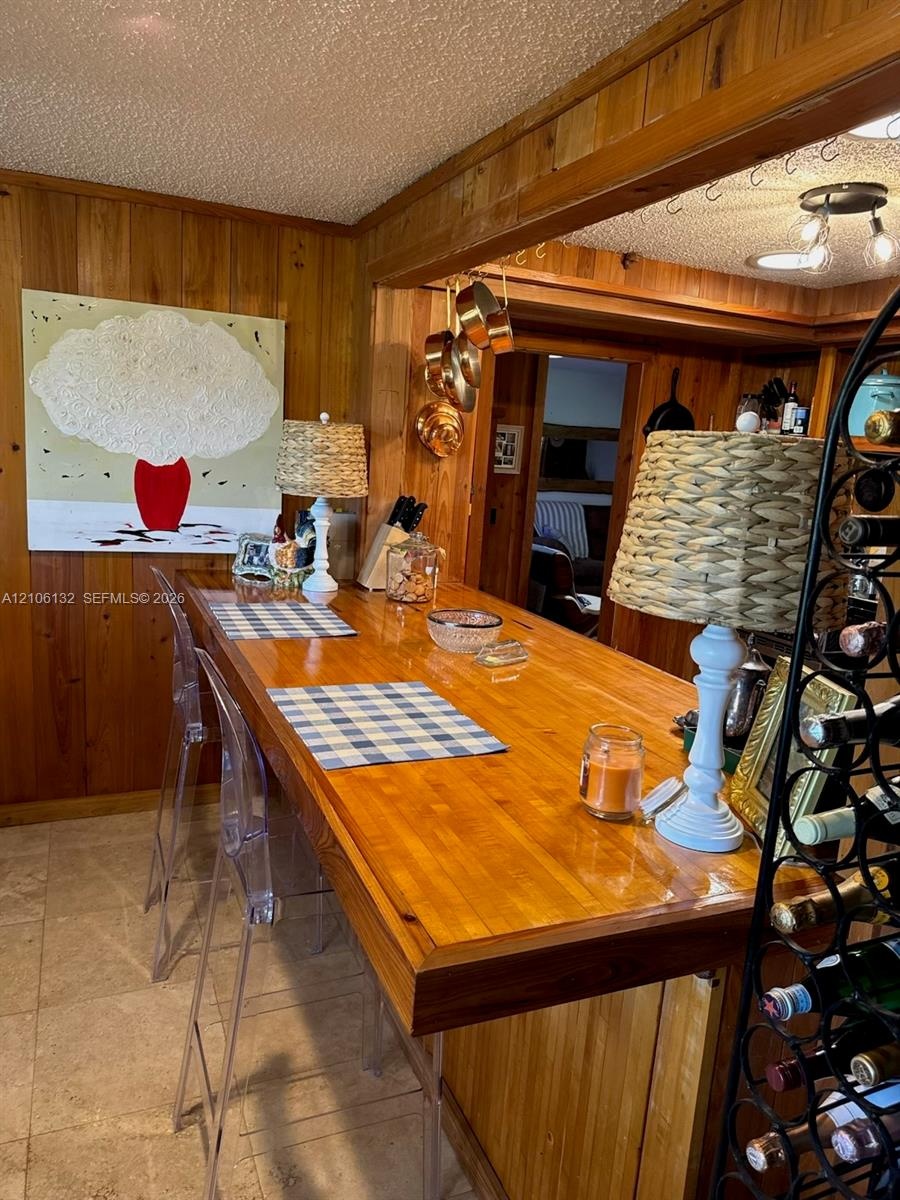 Built-in wood breakfast bar with a polished finish, vertical wood-paneled walls, tile flooring, and integrated ceiling lighting