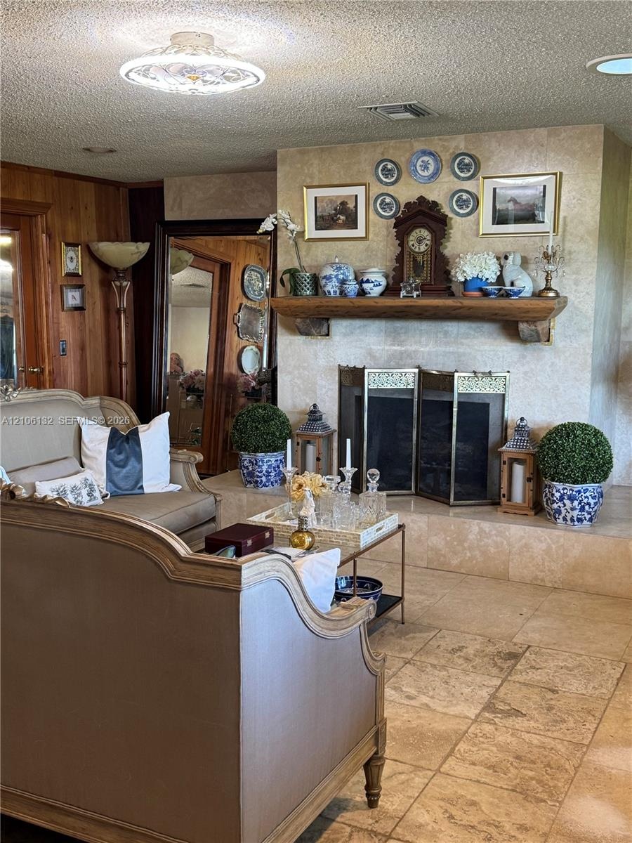Floor-to-ceiling stone fireplace surround with a natural wood mantel, stone tile flooring, and wood-paneled walls
