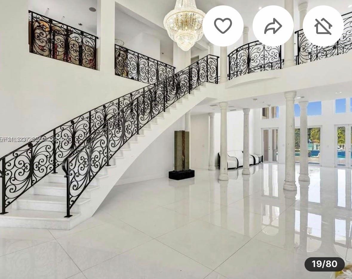 Grand foyer featuring polished tile flooring, decorative wrought-iron railings, a multi-tiered crystal chandelier, and soaring classical columns