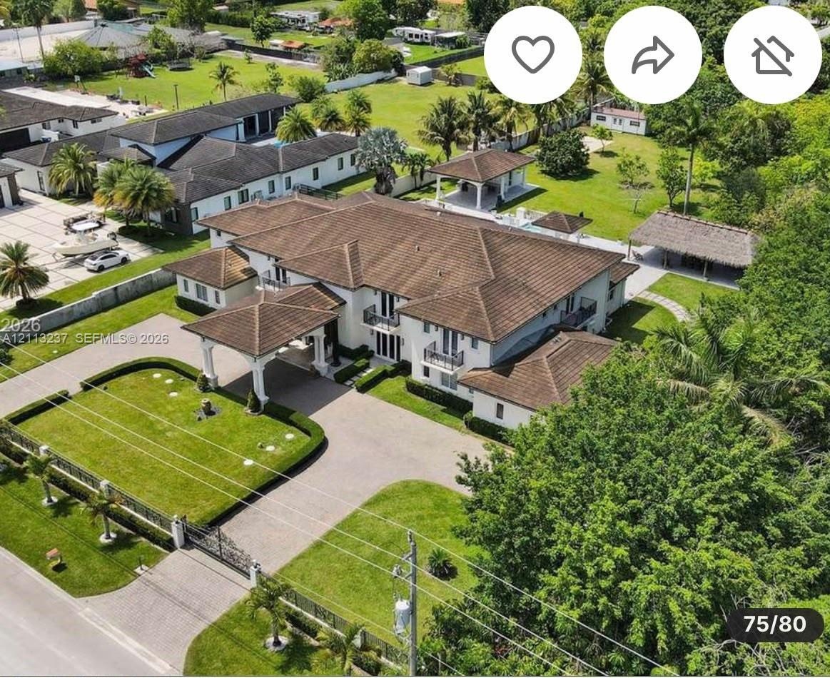 Expansive multi-structure estate featuring a porte-cochere, tile roof, gated entrance, structured landscaping, and a thatched-roof pavilion