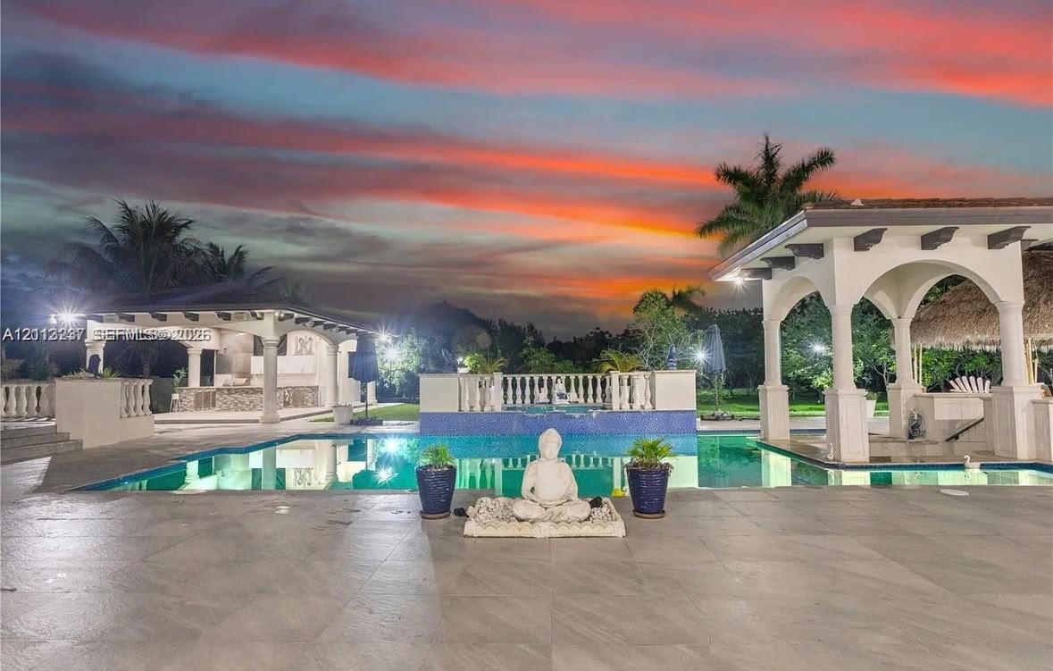 Swimming pool with mosaic tile border, covered outdoor pavilion, stone-finish patio, and balustrade railing