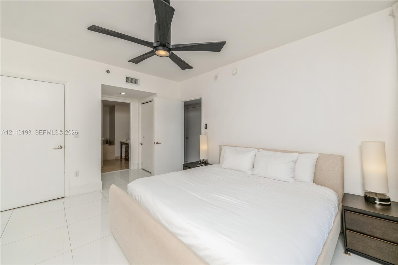 Interior room featuring polished white tile flooring, matte black ceiling fan with integrated lighting, and white smooth-finish interior doors