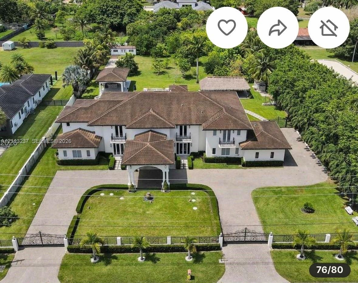 Expansive estate featuring a gated entrance, a paved circular driveway, a porte-cochère, a multi-gabled roofline, and an integrated outdoor pavilion