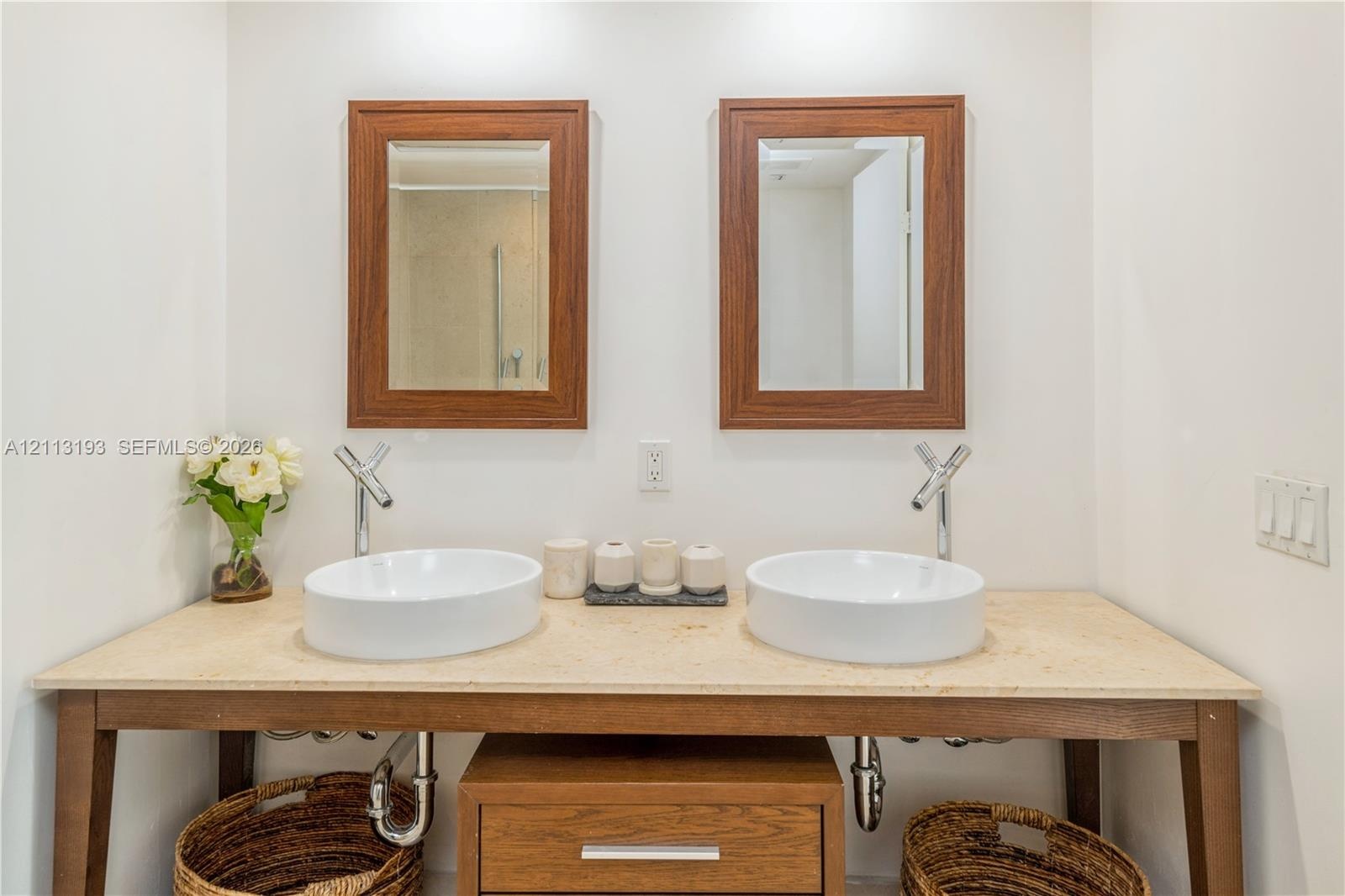 Double vanity featuring dual vessel sinks, stone-surface countertop, wood-finish console base, and paired wall-mounted wooden mirrors