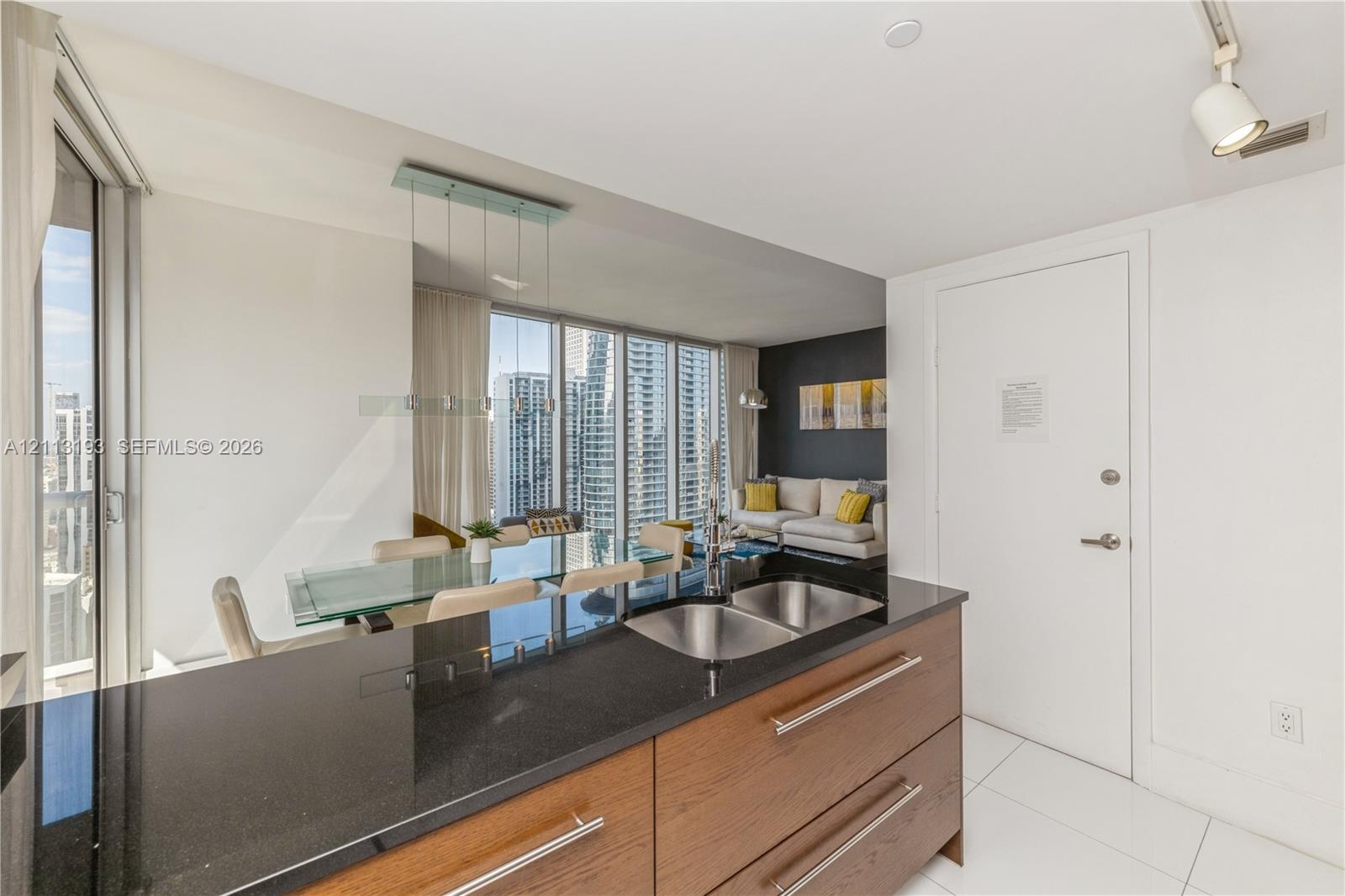 Kitchen featuring dark stone countertops, wood-finish cabinetry with stainless steel pulls, dual-basin undermount sink, porcelain tile flooring, and t