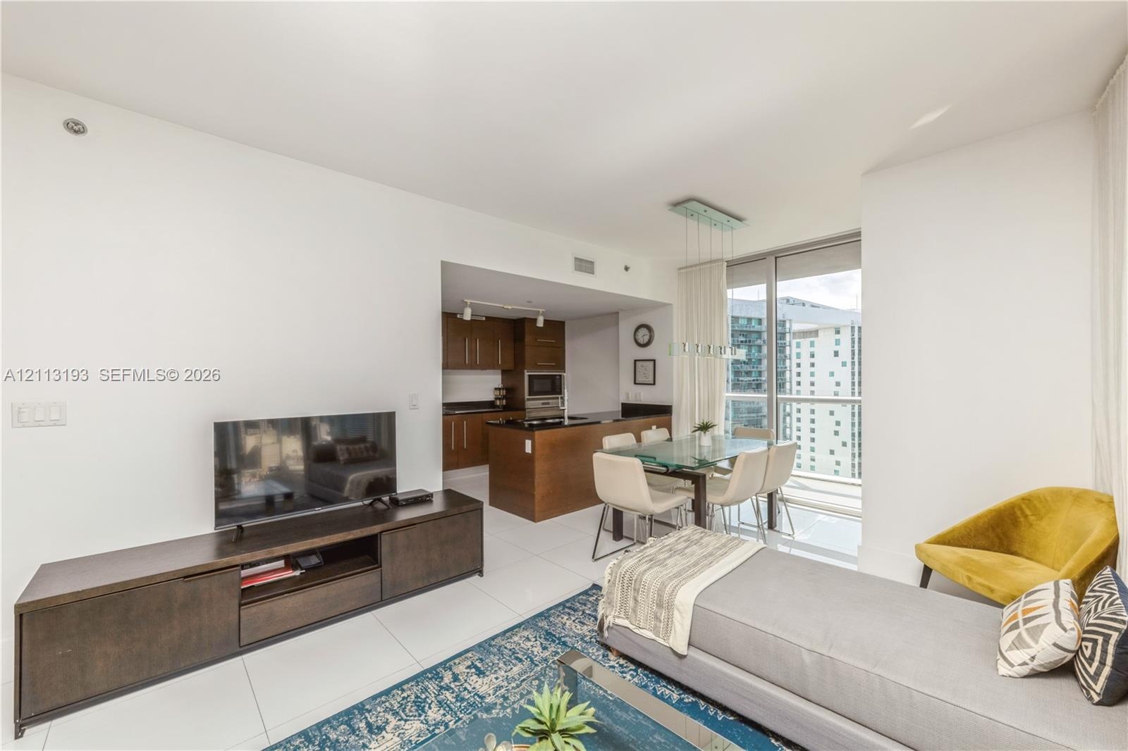 Open-concept living space featuring high-gloss tile flooring, floor-to-ceiling windows, and a kitchen with dark-finish wood cabinetry and a central is