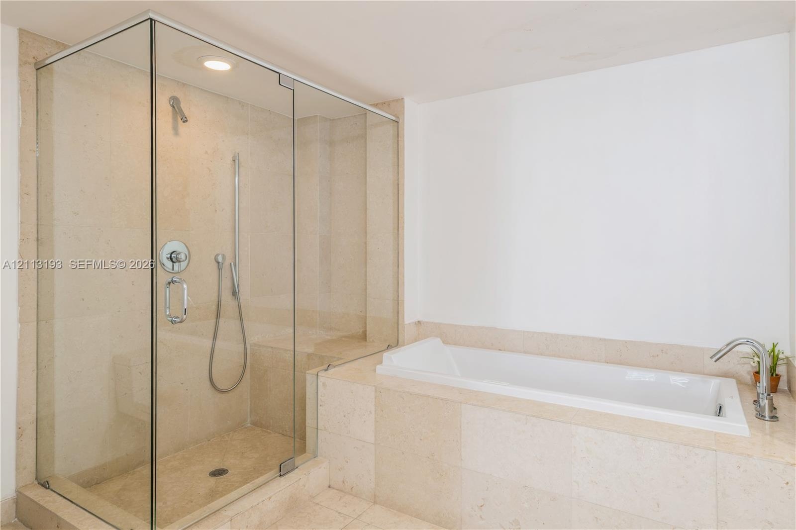 Walk-in glass-enclosed shower with stone-finish tiling and built-in bench, paired with a drop-in soaking tub featuring stone-finish surround and metal