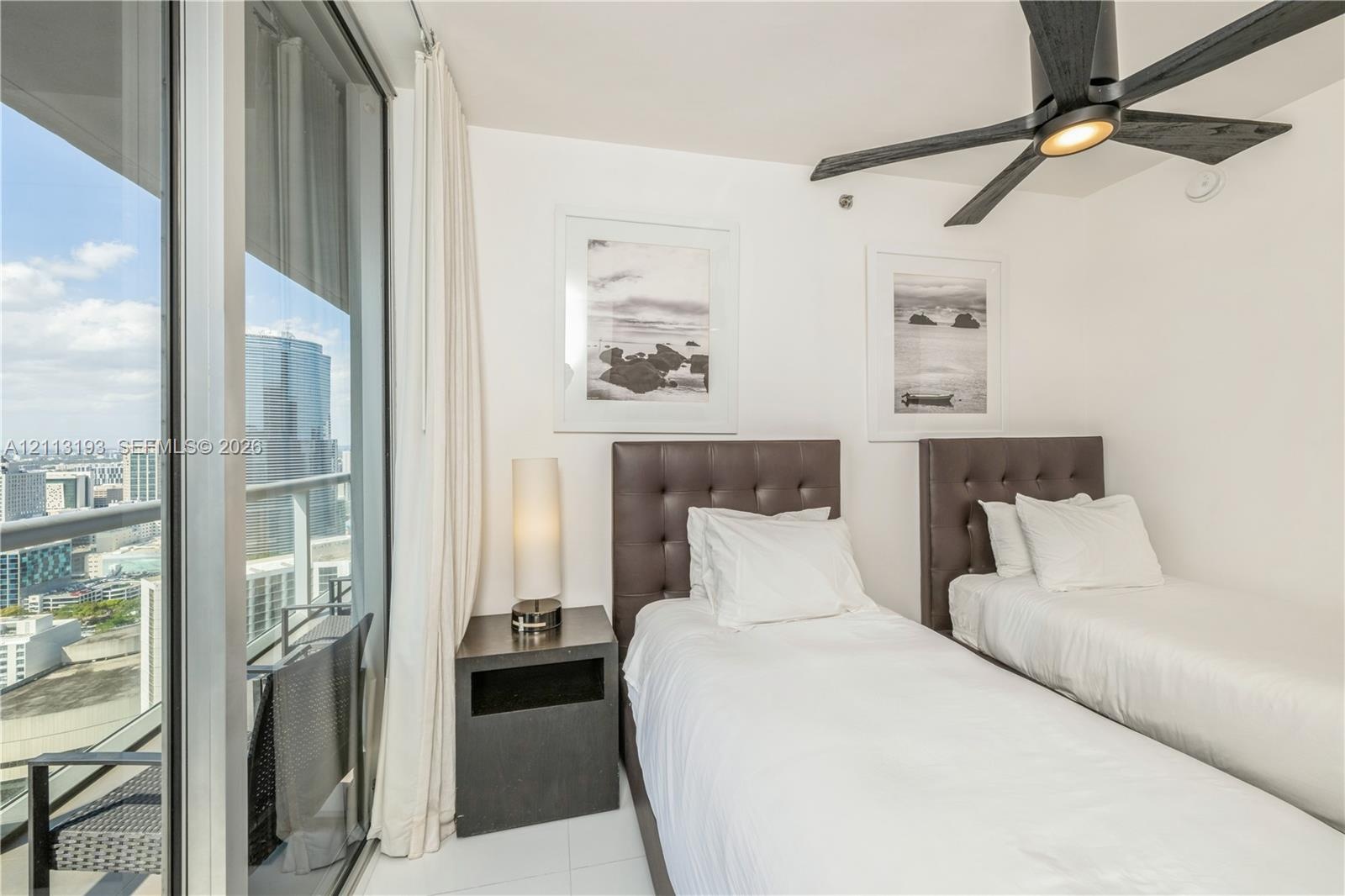 Floor-to-ceiling glass sliding doors, private balcony, matte black ceiling fan, and tile flooring