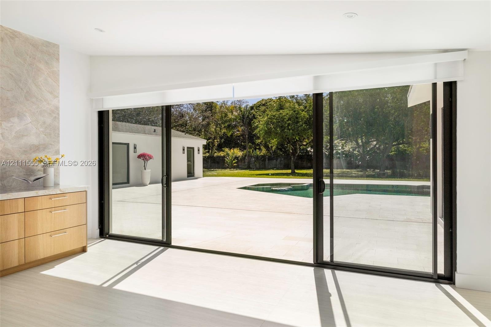 Floor-to-ceiling sliding glass doors, built-in natural wood cabinetry with stone countertop, large format light-toned tile flooring, concrete patio, a