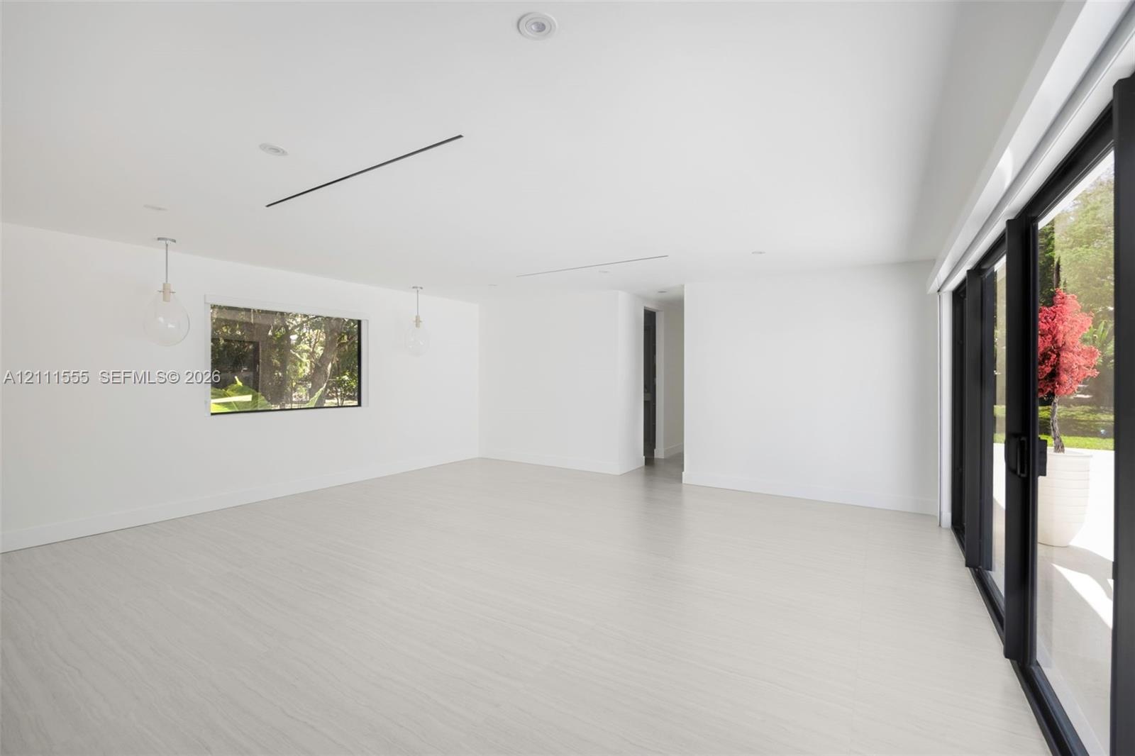 Open-concept interior with light-toned wood-finish flooring, recessed lighting, glass pendant fixtures, and floor-to-ceiling black-framed sliding glas