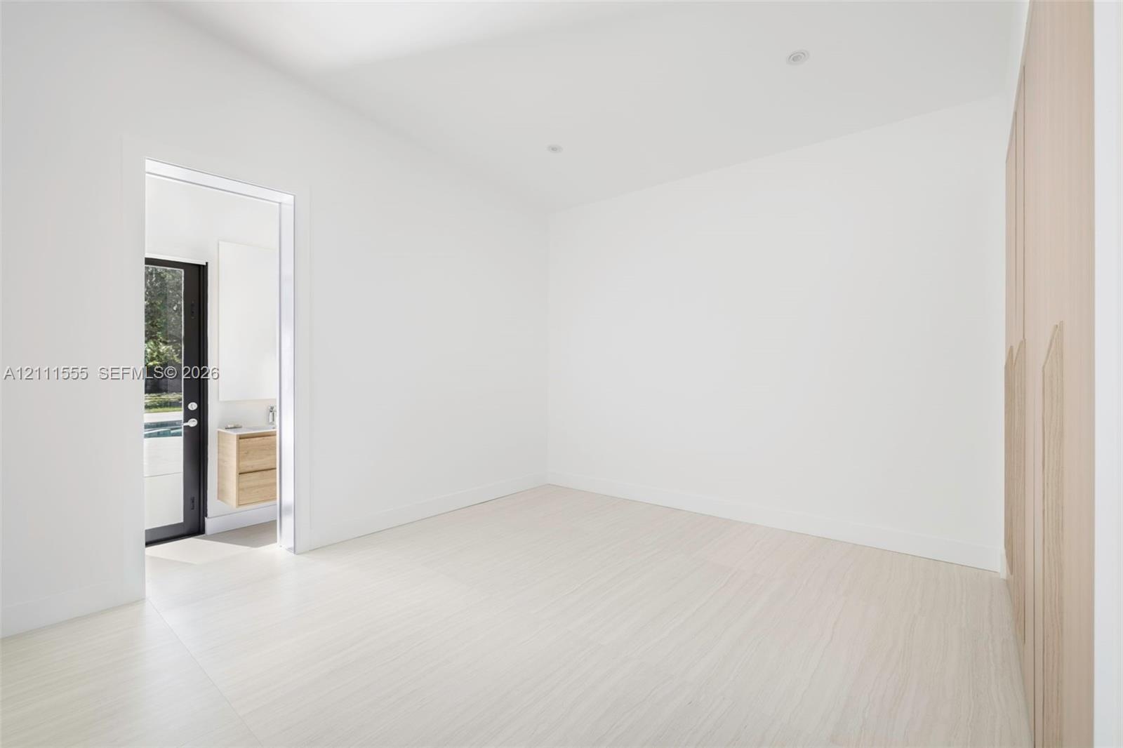 Minimalist room featuring wood-finish flooring, integrated floor-to-ceiling cabinetry, recessed lighting, and a glass-paneled exterior door