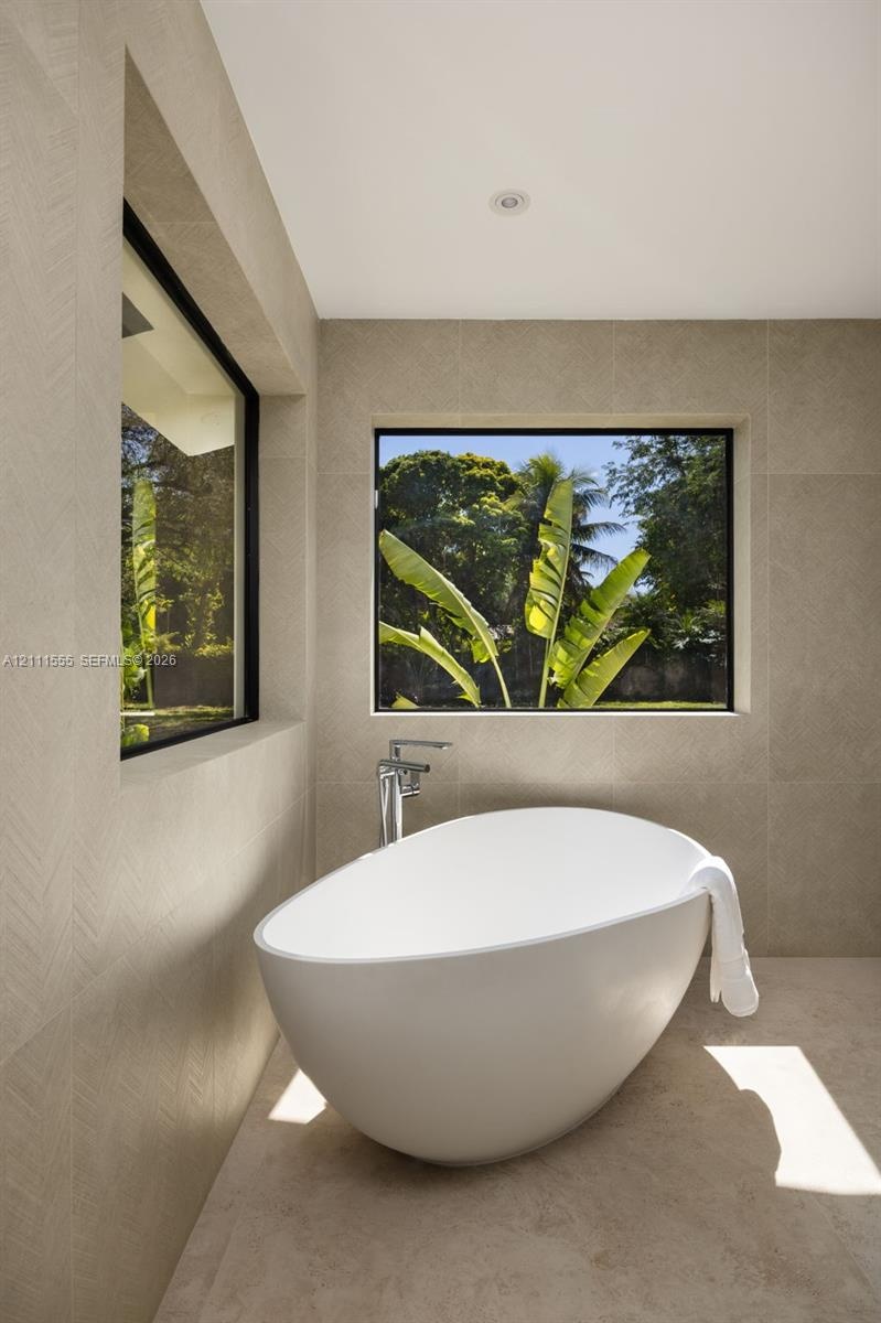 Freestanding soaking tub featuring a chrome floor-mounted faucet, set against large-format neutral tile walls with textured herringbone detailing and 