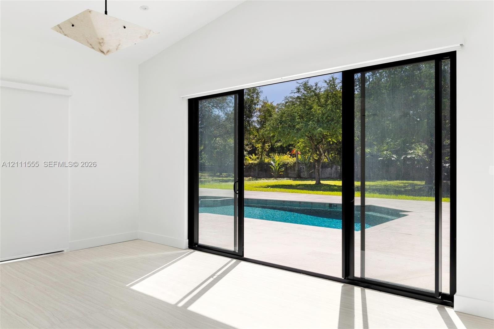 Vaulted ceiling, geometric pendant lighting, light-toned flooring, and expansive black-framed sliding glass doors opening to an outdoor swimming pool 