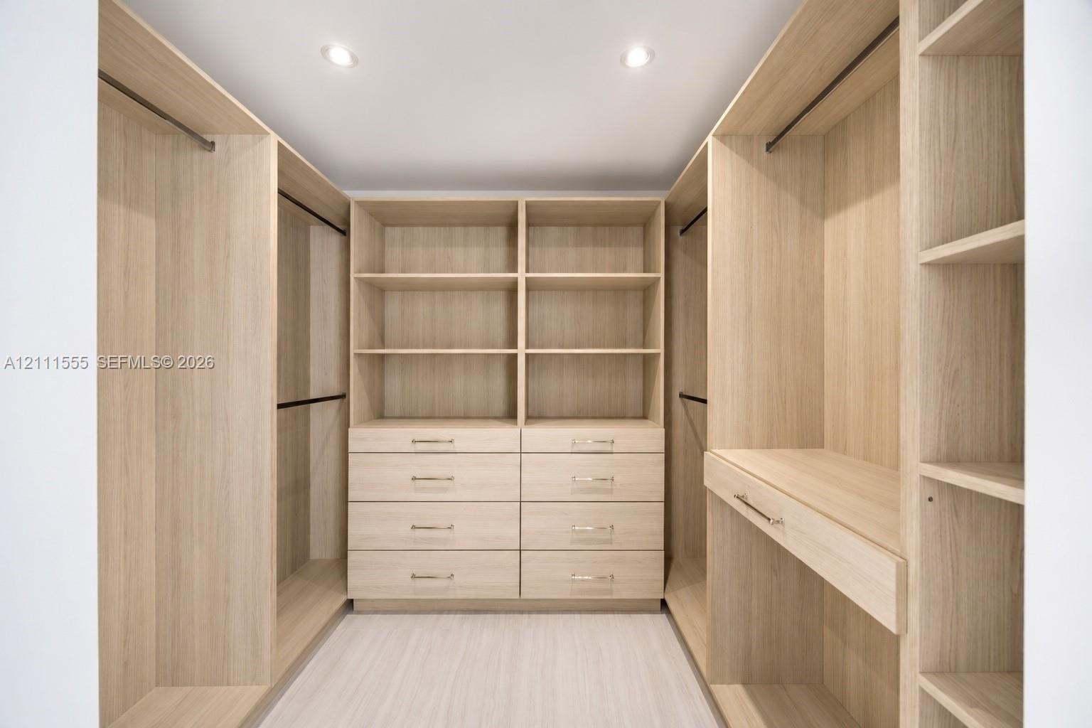 Primary Closet - His Custom wood-finish cabinetry featuring integrated shelving, dual hanging rods, built-in dresser drawers with metallic hardware, a