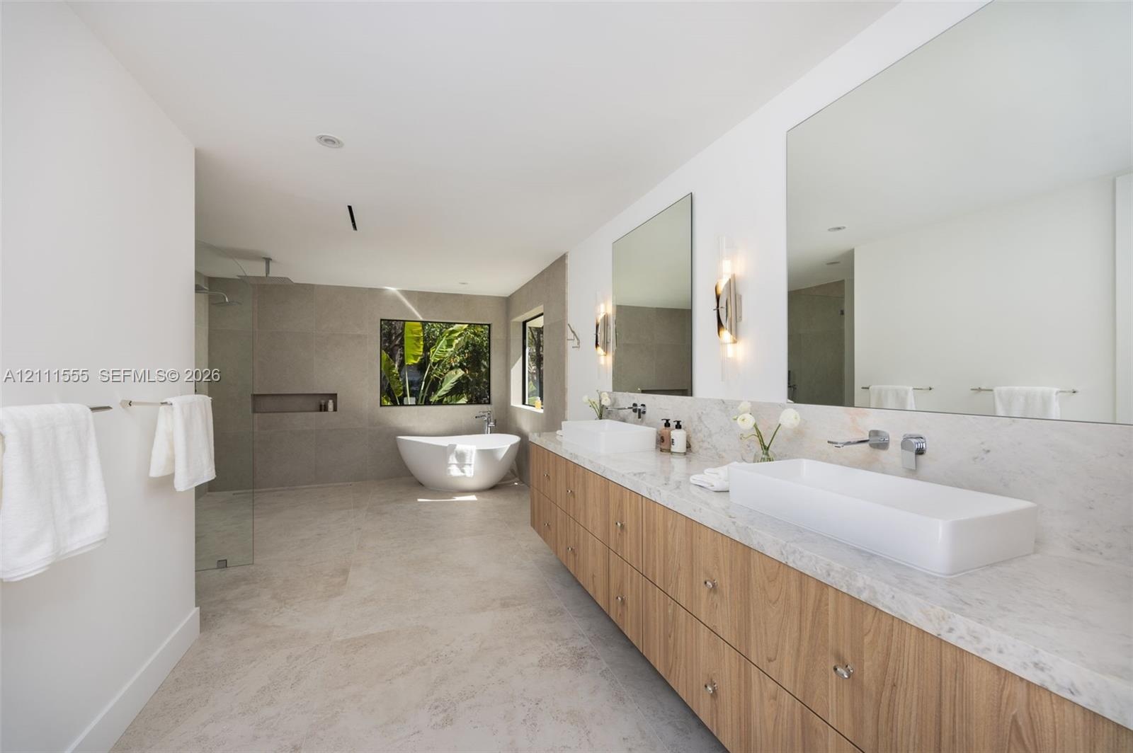 Floating dual vanity with stone-finish countertops, rectangular vessel sinks, wall-mounted faucets, large-format tile flooring, and a freestanding soa