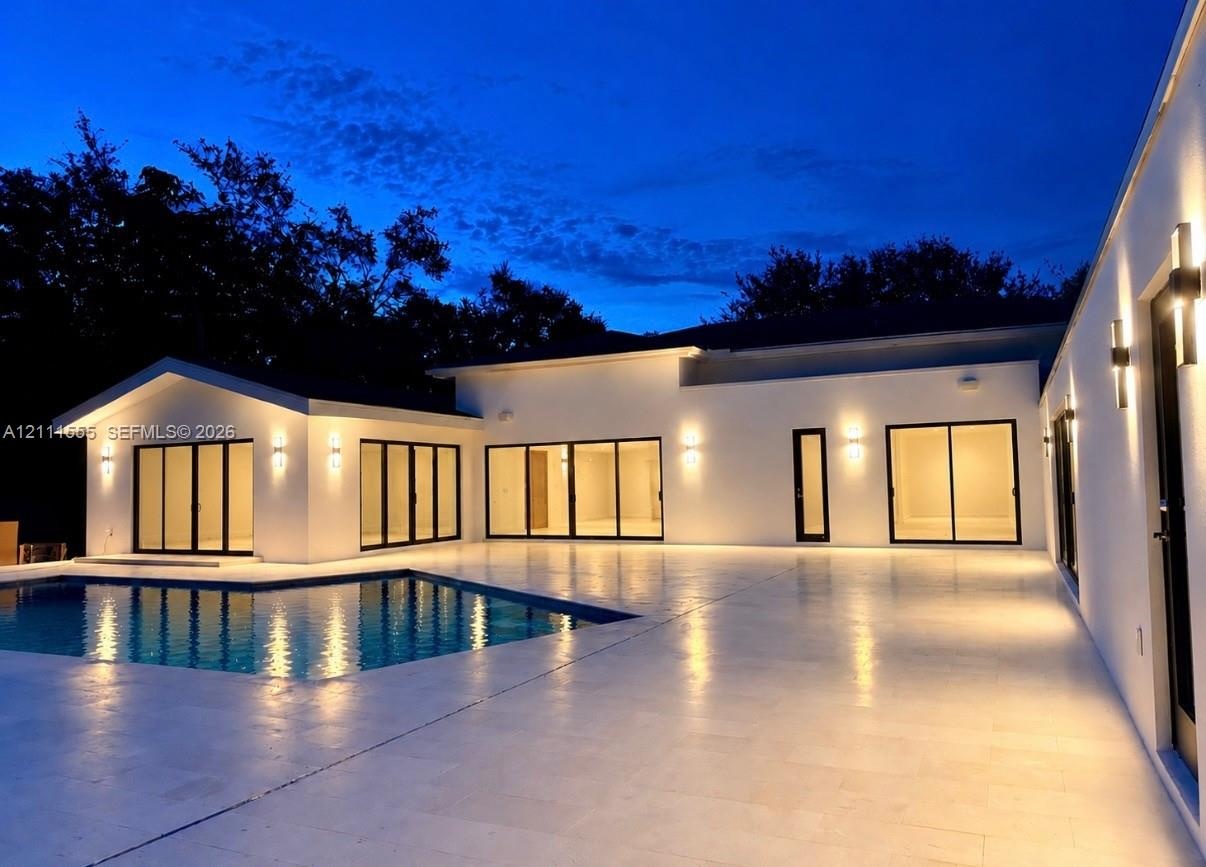 Contemporary exterior featuring smooth stucco finish, expansive stone patio, integrated wall-mounted lighting, multiple sliding glass door sets, and a