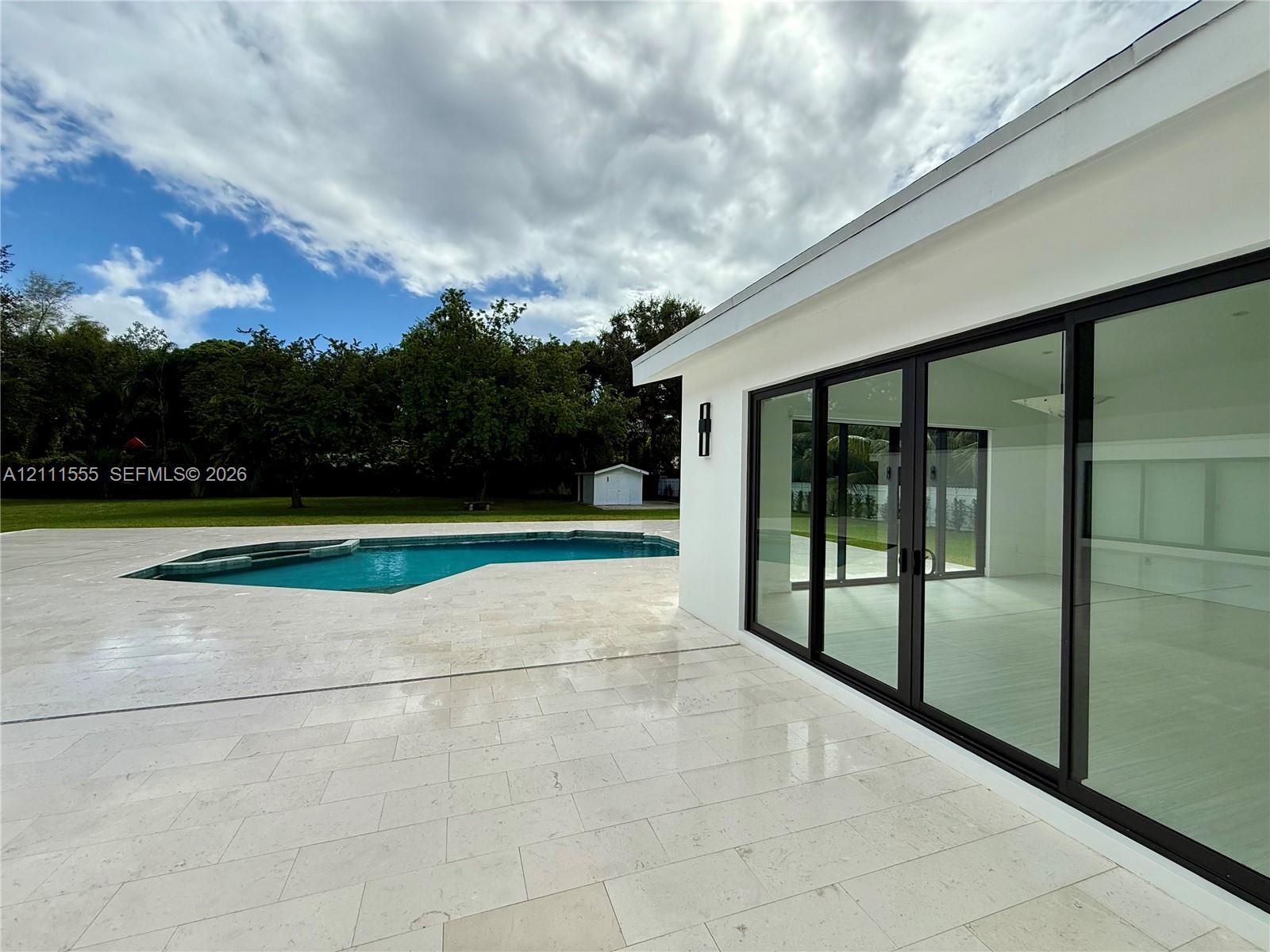 Backyard featuring stone patio, in-ground swimming pool, and expansive sliding glass doors with black framing