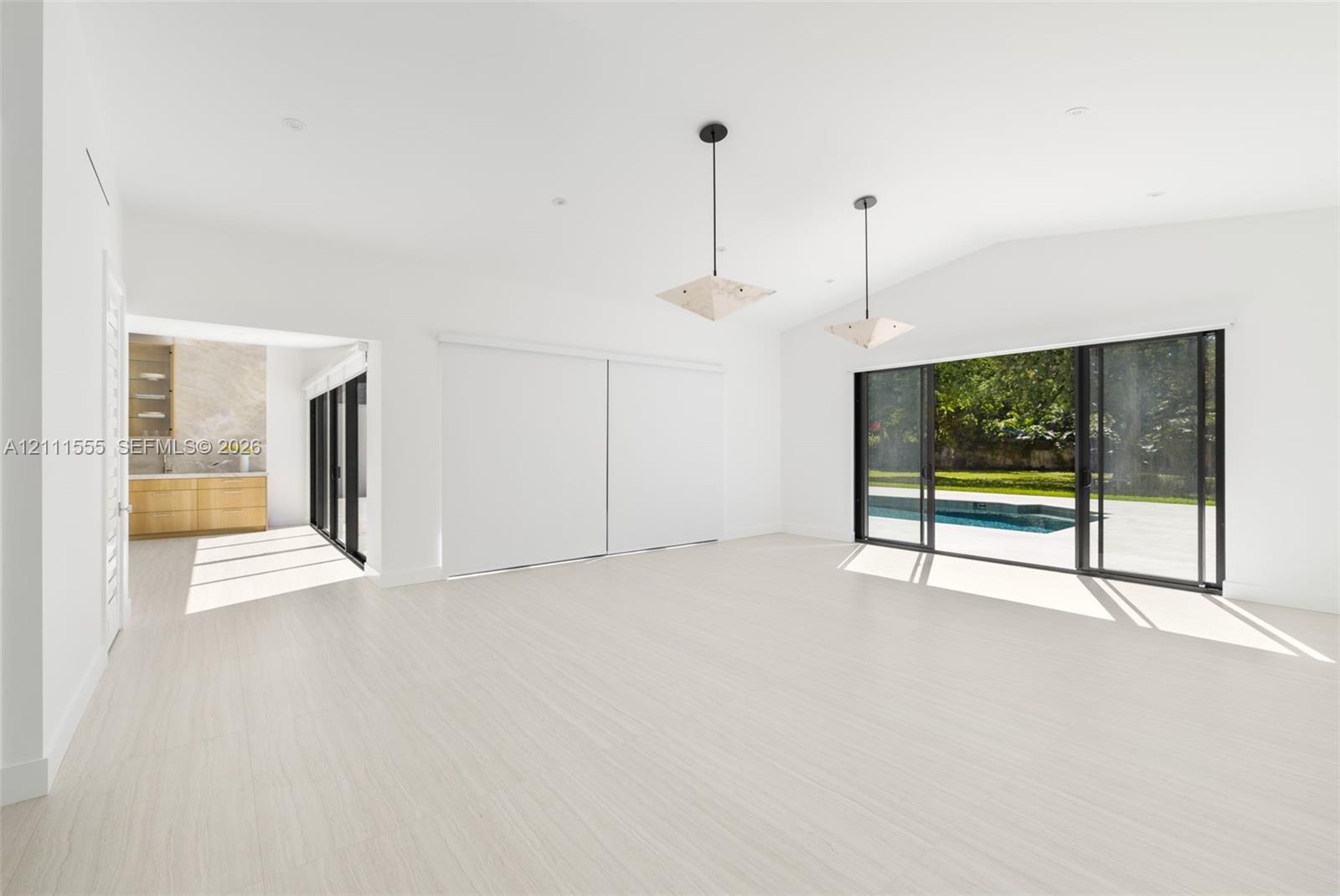 Open living area featuring vaulted ceilings, wood-finish flooring, dual geometric pendant lighting, and multi-panel sliding glass doors with exterior 