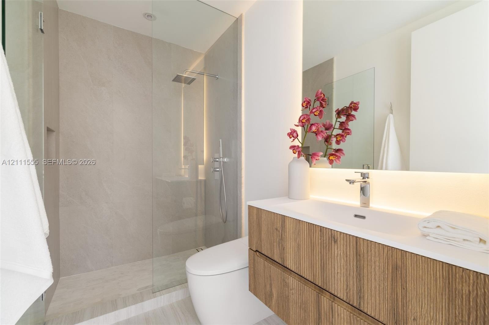 Floating wood-finish vanity with an integrated sink, walk-in glass-enclosed shower featuring large-format tile surround, rain-style showerhead, and in