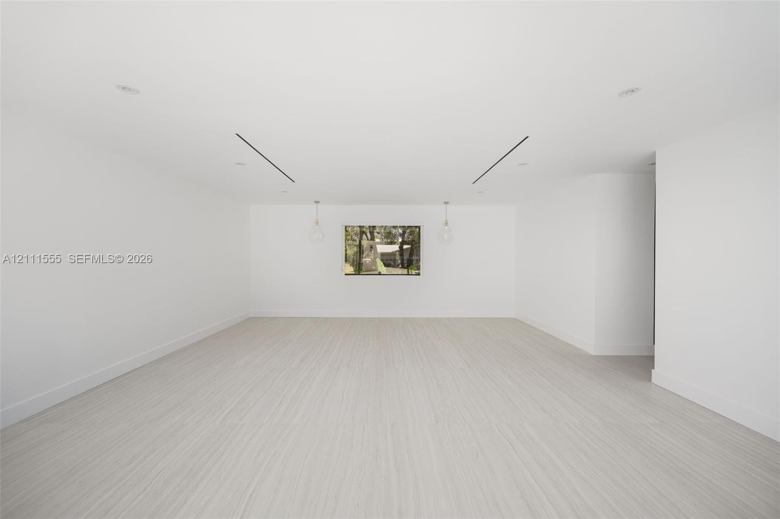 Neutral interior space featuring wood-finish flooring, recessed lighting, linear architectural ceiling accents, and dual pendant light fixtures