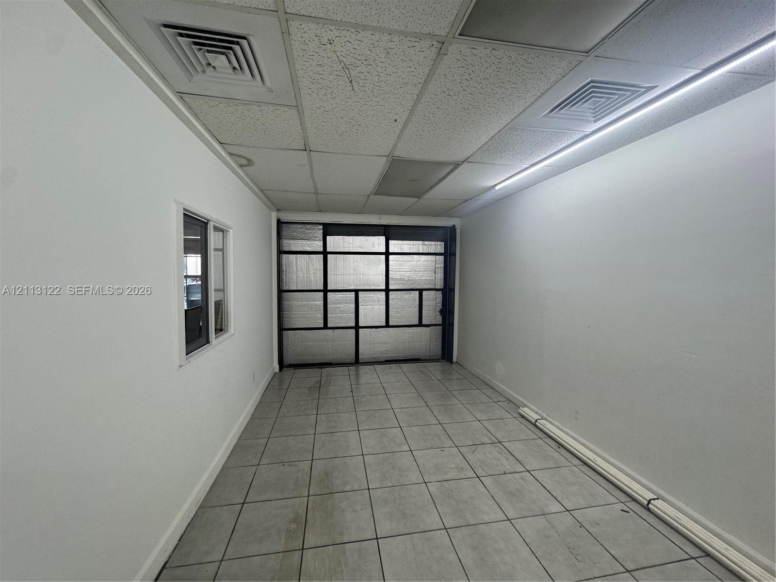 Interior space featuring tile flooring, white walls, a multi-pane glass window, and a drop ceiling with integrated linear lighting