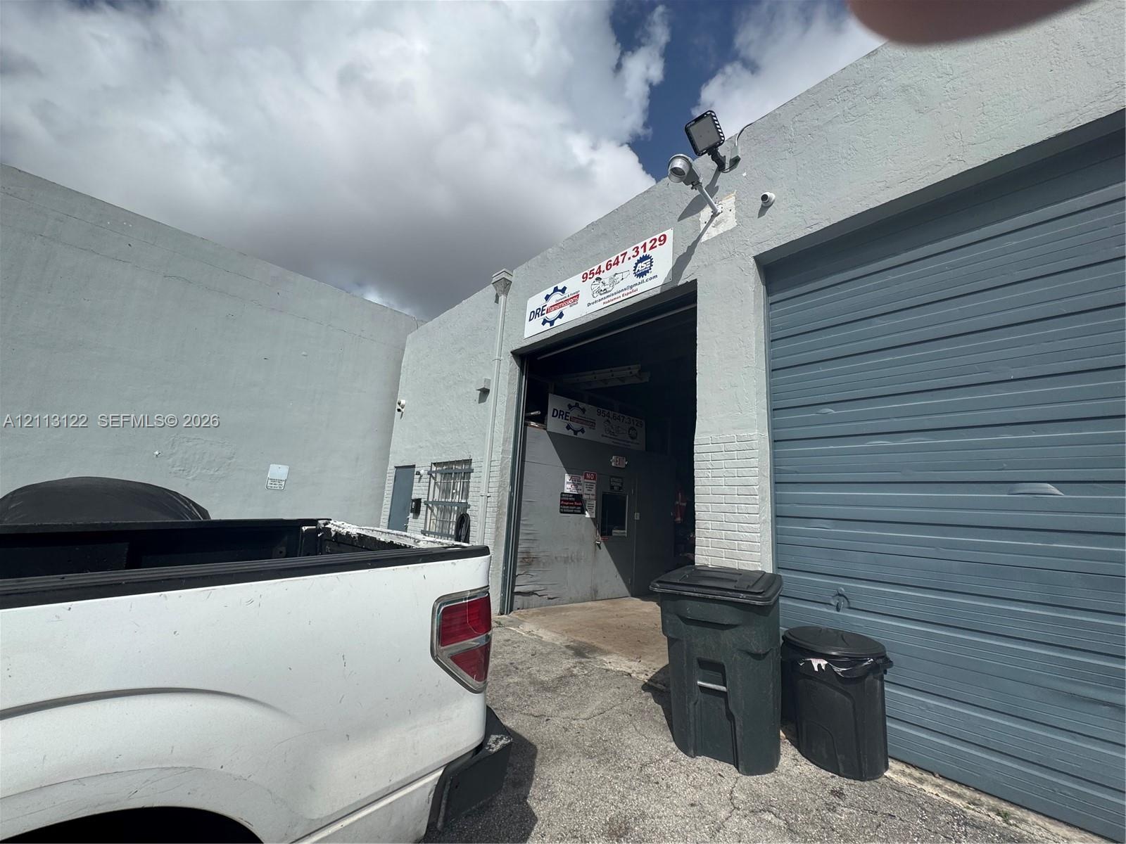 Commercial exterior featuring masonry construction, a high-clearance overhead roll-up door, and mounted exterior security lighting