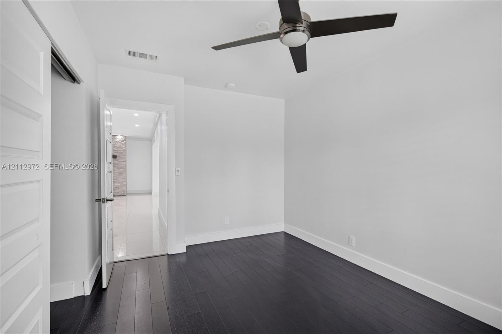 Room featuring dark wood-finish flooring, a multi-blade ceiling fan with integrated lighting, and a solid-core interior door