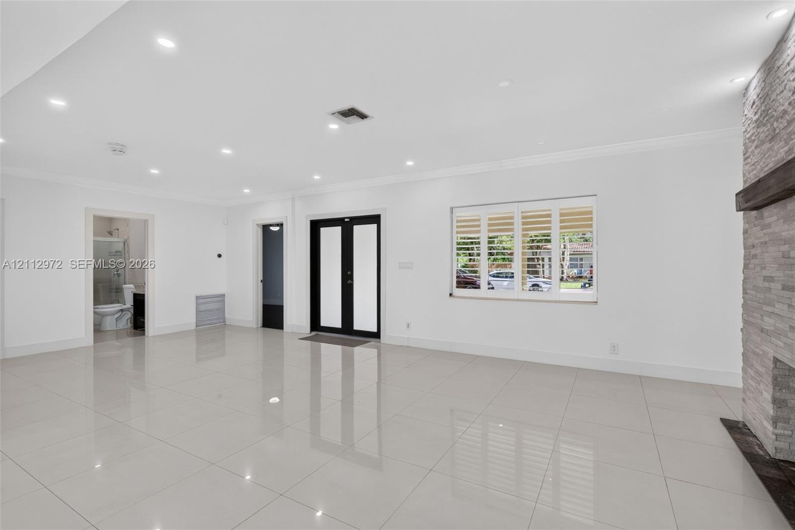 Large-format tile flooring, recessed ceiling lighting, stone-clad fireplace with a timber mantel, double-entry front door with glass insets, and windo
