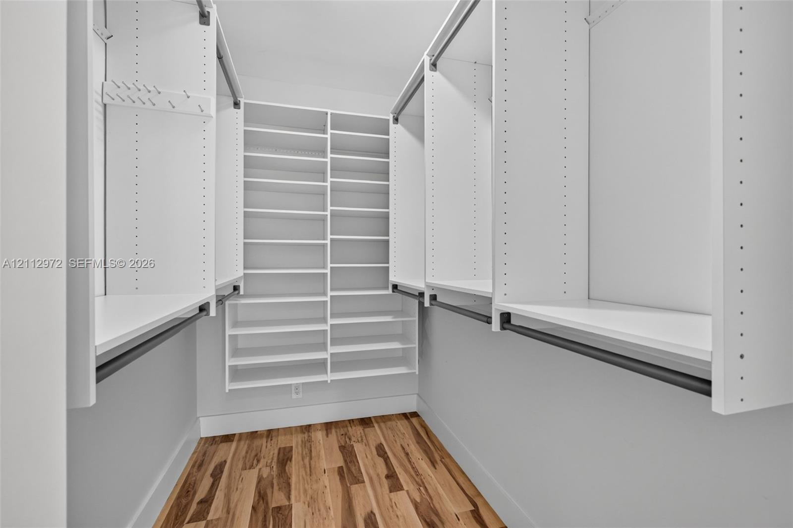 Walk-in closet featuring white built-in shelving, multiple hanging rods, and wood-finish flooring