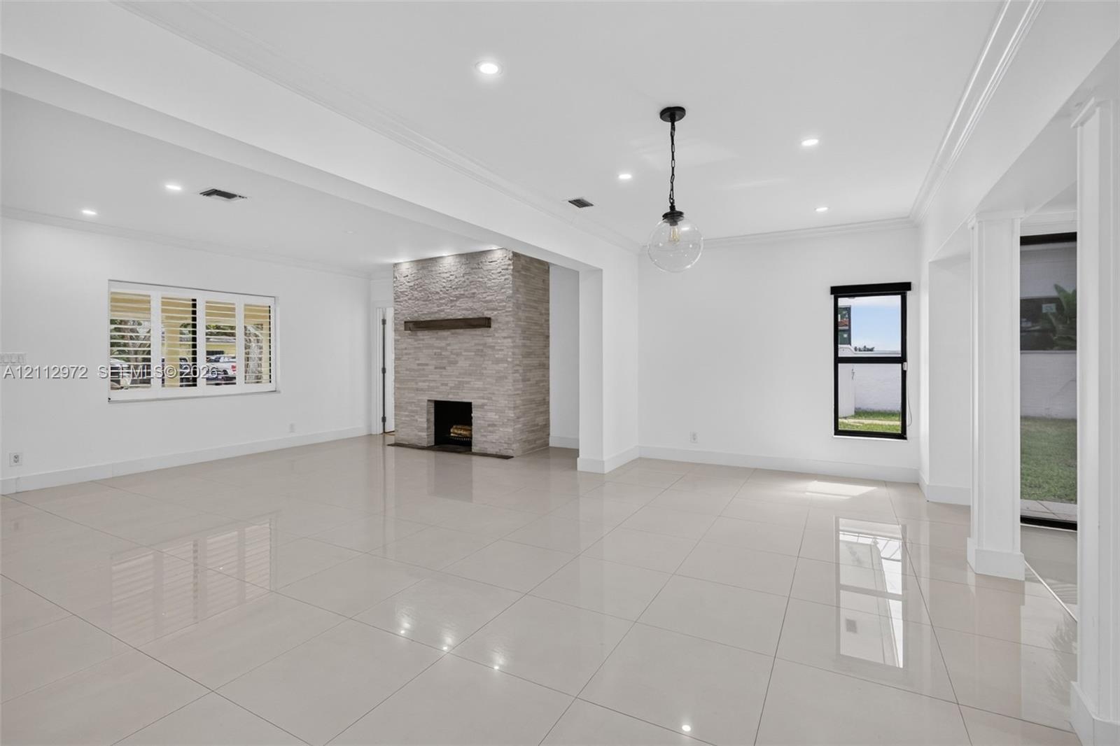 Open-concept interior featuring light-toned tile flooring, a floor-to-ceiling stacked stone fireplace with a wood mantel, recessed lighting, and a mod