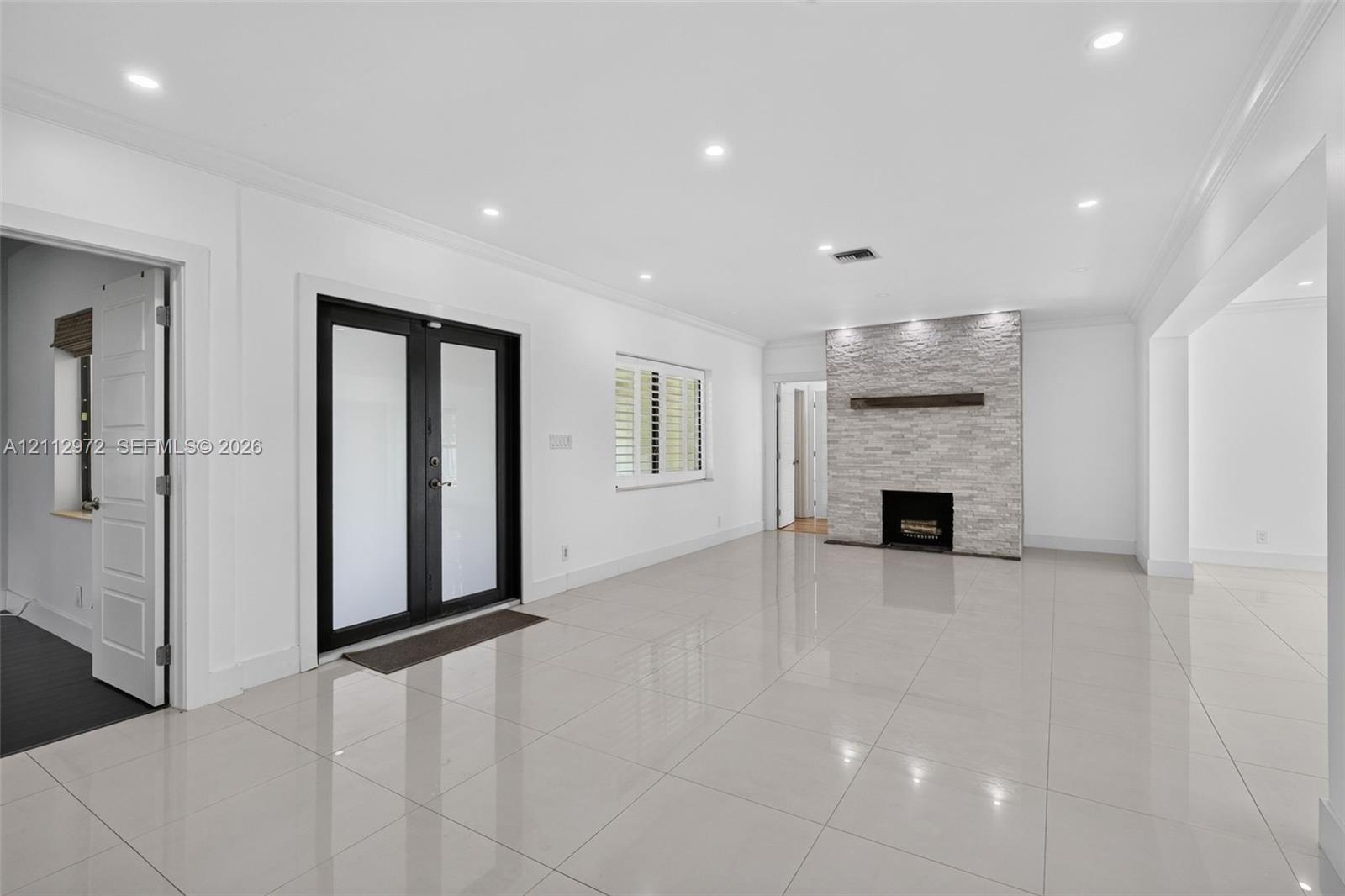 Large-format tile flooring, recessed ceiling lighting, stone-veneer fireplace with a wood mantel, and black-framed glass panel double doors