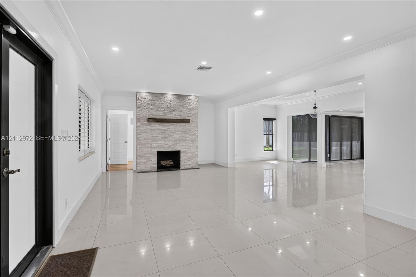 Open-concept interior featuring large-format polished tile flooring, stone-veneer fireplace with a wood mantel, recessed ceiling lighting, and floor-t