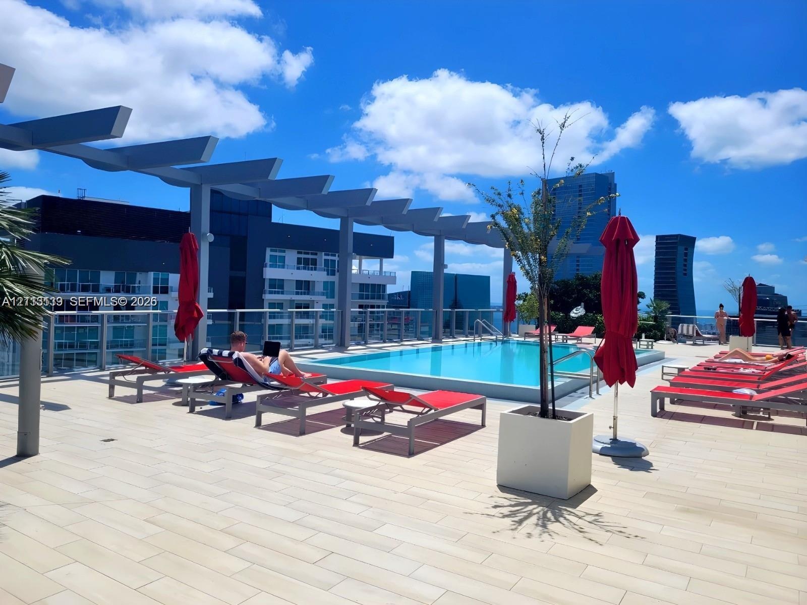 Rooftop terrace featuring an elevated swimming pool, metal pergola, tile flooring, and glass panel railing
